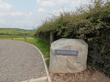 A large rock with a Weirglodd nameplate beside a gravel driveway and hedge at Weirglodd in Ruthin