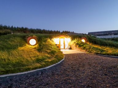 A grass covered earth house with round windows and a lit entrance at Weirglodd in Ruthin