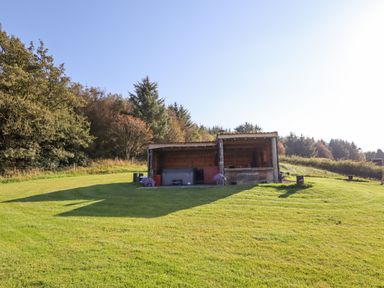 An outdoor wooden shelter on a grassy area with trees in the background at Weirglodd in Ruthin
