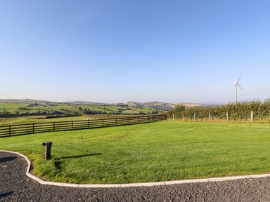 A fenced grassy field with a wind turbine and hills in the background at Weirglodd in Ruthin