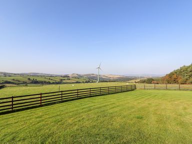 A grassy field with a wooden fence wind turbines and hills in the background at Weirglodd in Ruthin
