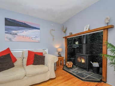 A living room with a beige sofa and cushions near a black wood stove with a wooden mantle at Stone's Throw Cottage in Launceston
