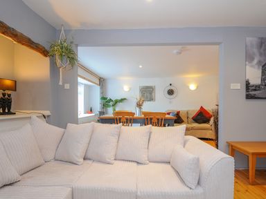 A living room with a white sofa wooden dining table and chairs and a plant at Stone's Throw Cottage in Launceston