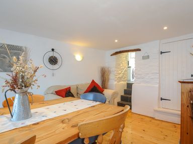 A dining area with a wooden table and chairs a sofa with cushions a wall clock and stairs at Stone's Throw Cottage in Launceston