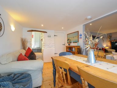 A dining area with a wooden table and chairs beside a living room with sofas and cushions at Stone's Throw Cottage in Launceston