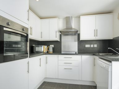 A kitchen with white cabinets black countertops a built-in oven a microwave a kettle a sink and a dishwasher at Stone's Throw Cottage in Launceston