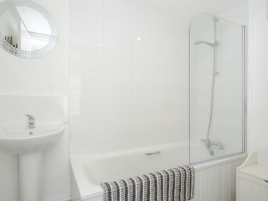 A bathroom with a bathtub shower combination a pedestal sink a round mirror and a striped towel on the bathtub at Stone's Throw Cottage in Launceston