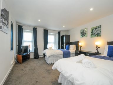 A bedroom with two single beds a television on a stand and black curtains at Stone's Throw Cottage in Launceston