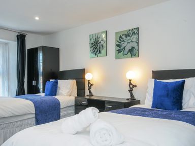 A bedroom with two single beds with blue cushions and throws a black wardrobe a black bedside table with lamps and floral wall art at Stone's Throw Cottage in Launceston