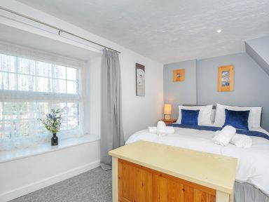 A bedroom with a double bed blue pillows rolled towels a window with curtains and a wooden chest at Stones Throw Cottage in Launceston