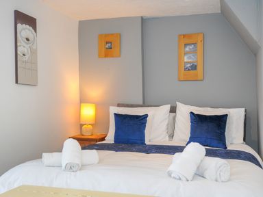 A bedroom with a double bed with white sheets blue pillows and rolled towels with a nightstand lamp and framed pictures on the walls at Stone's Throw Cottage in Launceston