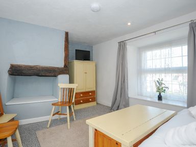 A small sitting room with a wooden chair a wooden table a cabinet with a TV and a window with curtains at Stone's Throw Cottage in Launceston