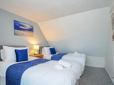 A bedroom with two single beds side by side with white bedding and blue accents and a lamp on a wooden nightstand at Stone's Throw Cottage in Launceston