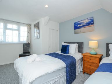 A bedroom with two single beds a wooden bedside table with a lamp a black chair and a window at Stone's Throw Cottage in Launceston