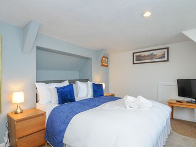 A bedroom with a bed with blue pillows and blanket two wooden bedside tables with lamps a TV on a wooden table and framed pictures on walls at Stones Throw Cottage in Launceston