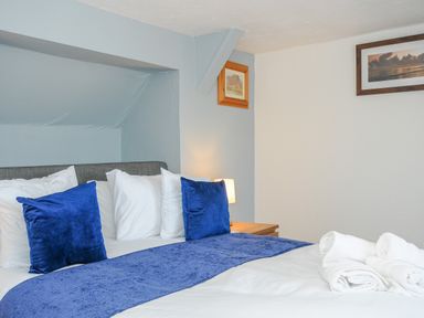 A bedroom with a bed with blue pillows and white linens and two framed pictures on the walls at Stones Throw Cottage in Launceston