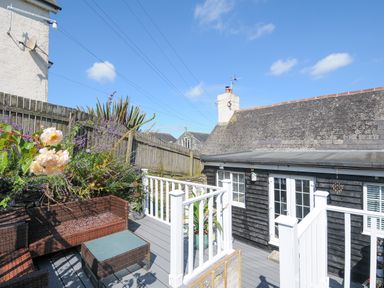 An outdoor deck with wicker furniture and plants next to a black wooden house at Stone's Throw Cottage in Launceston