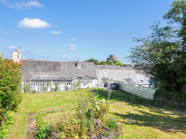 A garden with grass and plants overlooking rooftops and a small castle in the distance at Stone's Throw Cottage in Launceston