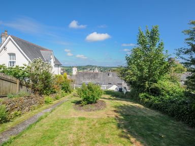 A garden with grass and bushes between houses with a distant view of rooftops at Stone's Throw Cottage in Launceston