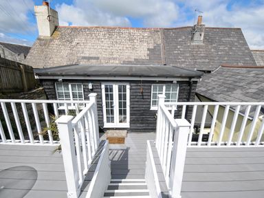 An outdoor deck with white railings and stairs leading to a black wooden building with white framed windows and double doors at Stone's Throw Cottage in Launceston