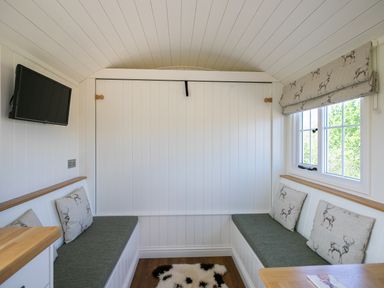 A small sitting area with built-in benches and cushions under a window with patterned blinds at Strathmore Burnside near Forfar