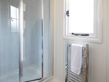 A bathroom with a glass shower enclosure a white towel on a chrome heated towel rail and a window at Strathmore Burnside near Forfar