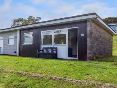 A small single-story house with dark wood siding and stone wall on a grassy slope at Florence's Nest in Dartmouth
