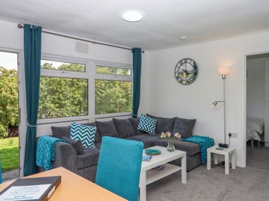 A living room with a gray sofa blue cushions a white table a floor lamp and a wall clock at Florences Nest in Dartmouth