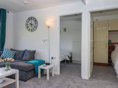 A living area with a grey sofa cushions and a lamp adjacent to two doorways showing bedrooms at Florence's Nest in Dartmouth