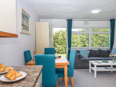 A dining area with turquoise chairs next to a living room with a gray sofa and large windows at Florences Nest in Dartmouth