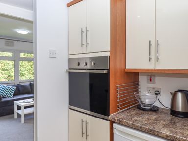 A kitchen corner with an oven built into cabinets and a countertop with a kettle and glass bowl near a living room with a sofa and coffee table at Florences Nest in Dartmouth