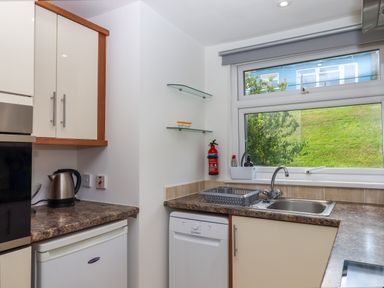 A kitchen with a sink dishwasher kettle and window showing outside at Florences Nest in Dartmouth