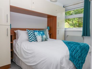 A bedroom with a double bed white bedding blue decorative pillows blue throw blanket built in white cabinets and a window with blue curtains at Florences Nest in Dartmouth