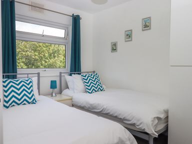 A bedroom with two single beds a window with blue curtains and a small bedside table with a lamp at Florences Nest in Dartmouth