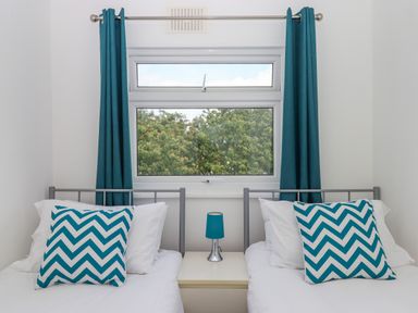 A bedroom with two single beds a bedside table with a lamp and a window with curtains at Florence's Nest in Dartmouth