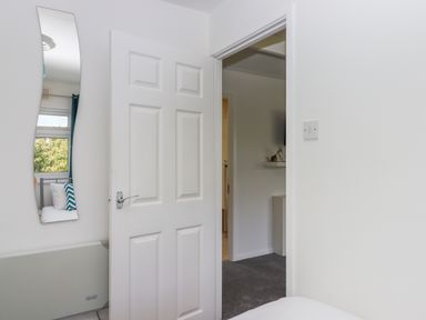 A partially open white door revealing another room with white walls and a gray carpet with a wall-mounted flat screen TV at Florence's Nest in Dartmouth