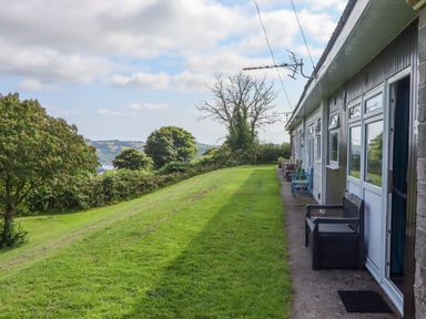 A row of outdoor benches along a building with grassy lawn and trees in the background at Florences Nest in Dartmouth