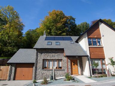 A house with stone and wood exterior with solar panels on the roof surrounded by trees at The Arthouse in Ambleside