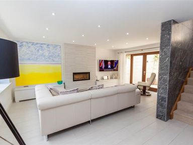 A living room with a white sectional sofa a fireplace and a television near wooden doors at The Arthouse in Ambleside