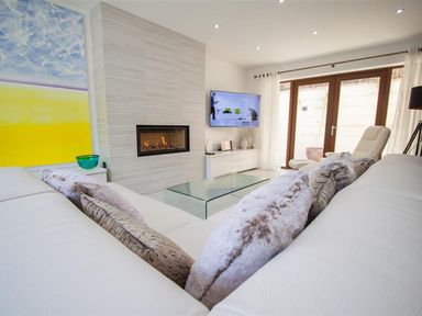 A living room with a fireplace wall mounted tv glass coffee table and white sofa with cushions at The Arthouse in Ambleside