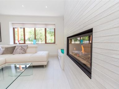 A living room with a white sectional sofa glass coffee table and a modern fireplace at The Arthouse in Ambleside