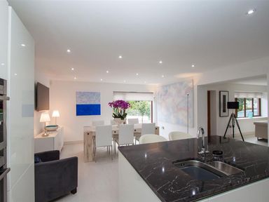 A dining area with a table and white chairs and a kitchen island with a sink in a modern open plan space at The Arthouse in Ambleside