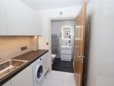 A utility room with a washing machine and sink leading to a bathroom with a sink and towel radiator at The Arthouse in Ambleside