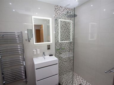 A bathroom with a sink cabinet mirror towel rail and a shower area with mosaic tiles at The Arthouse in Ambleside