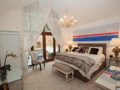 A bedroom with large bed, chandelier, armchair, and glass doors with sheer curtains at The Arthouse in Ambleside