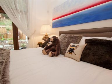 A bedroom with a bed with a teddy bear and decorative pillows next to a lamp and curtains at The Arthouse in Ambleside
