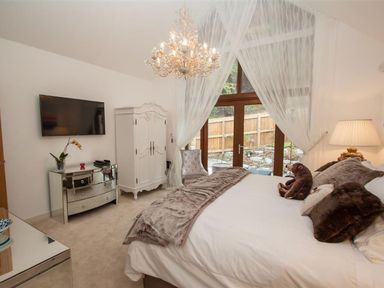 A bedroom with a bed pillows and a stuffed bear next to a window with sheer curtains and a chandelier at The Arthouse in Ambleside