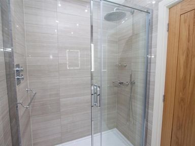 A bathroom shower area with glass doors a large showerhead and wooden door at The Arthouse in Ambleside