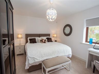A bedroom with a large bed two nightstands with lamps a bench a round wall mirror a window with a blue vase and a desk at The Arthouse in Ambleside