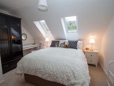 A bedroom with a bed under two skylight windows bedside tables with lamps a black wardrobe and a desk at The Arthouse in Ambleside